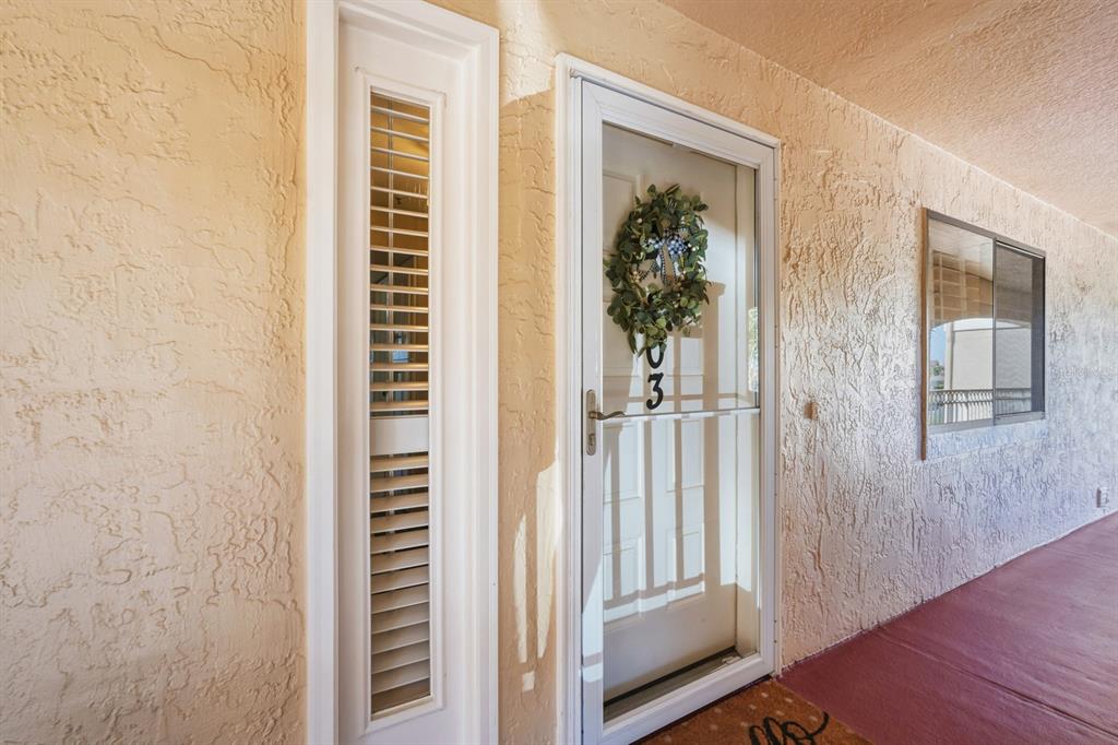 A white front door with a storm door and a side window on a stucco wall — 458 BOUCHELLE DRIVE UNIT 203, NEW SMYRNA BEACH, FL
