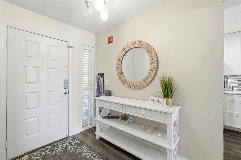 A white console table sits beneath a round mirror in an entryway with wood flooring — 458 BOUCHELLE DRIVE UNIT 203, NEW SMYRNA BEACH, FL