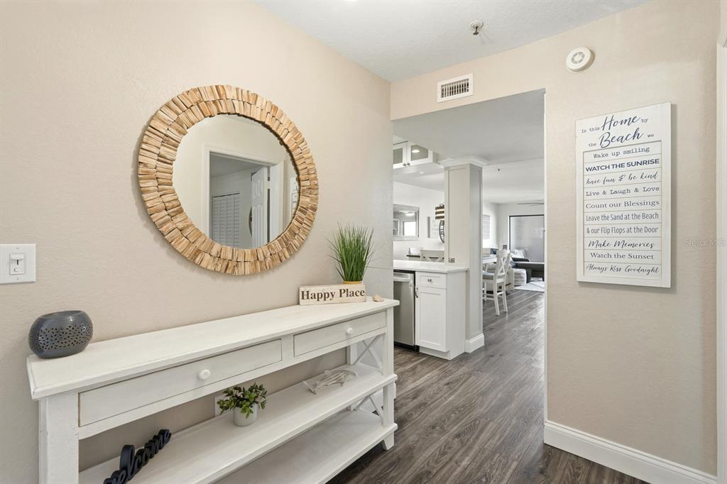 A white console table with a round wood-framed mirror sits in a neutral-toned entryway — 458 BOUCHELLE DRIVE UNIT 203, NEW SMYRNA BEACH, FL