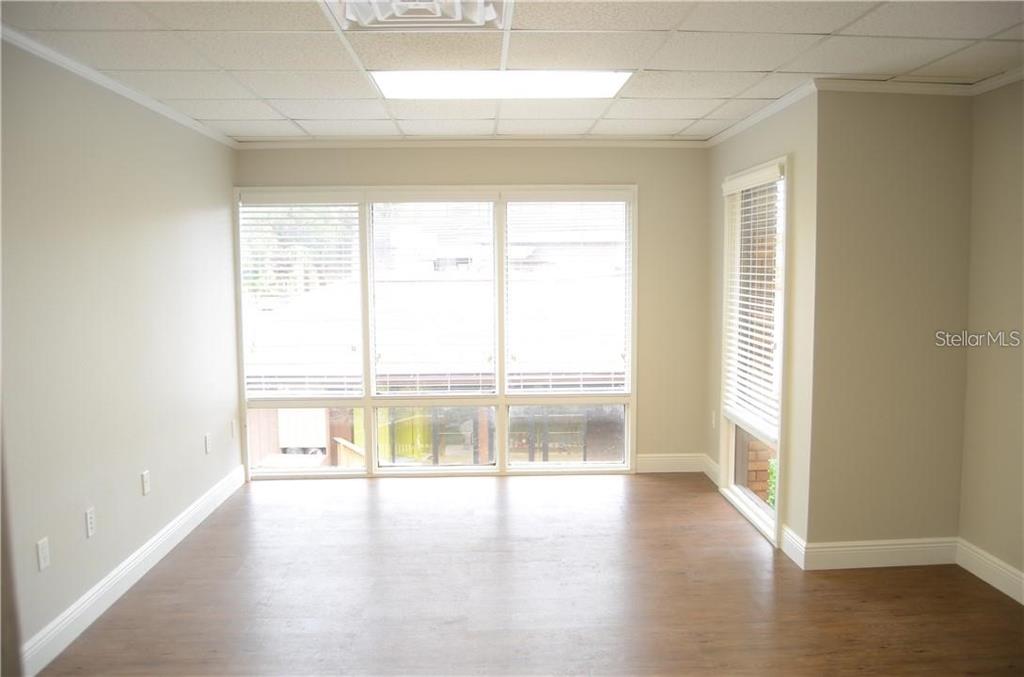 An empty room with wood-look flooring, beige walls, a drop ceiling, and large windows — 241 RUBY AVENUE UNIT 211, KISSIMMEE, FL