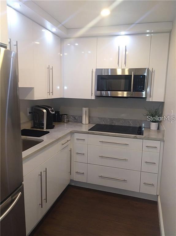 A modern kitchen features white glossy cabinets, stainless steel appliances, and dark wood flooring — 241 RUBY AVENUE UNIT 211, KISSIMMEE, FL