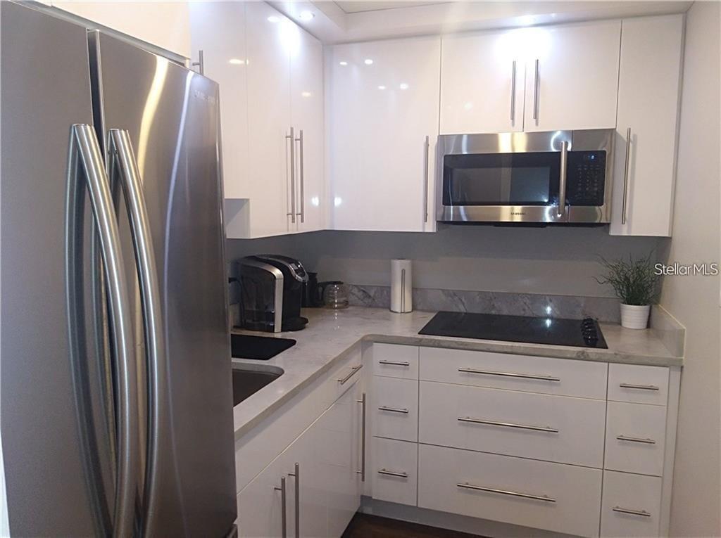 A modern kitchen features white high-gloss cabinets, stainless steel appliances, and gray stone countertops — 241 RUBY AVENUE UNIT 211, KISSIMMEE, FL