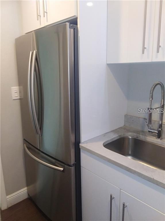 A stainless steel refrigerator stands next to a kitchen sink with white cabinets — 241 RUBY AVENUE UNIT 211, KISSIMMEE, FL