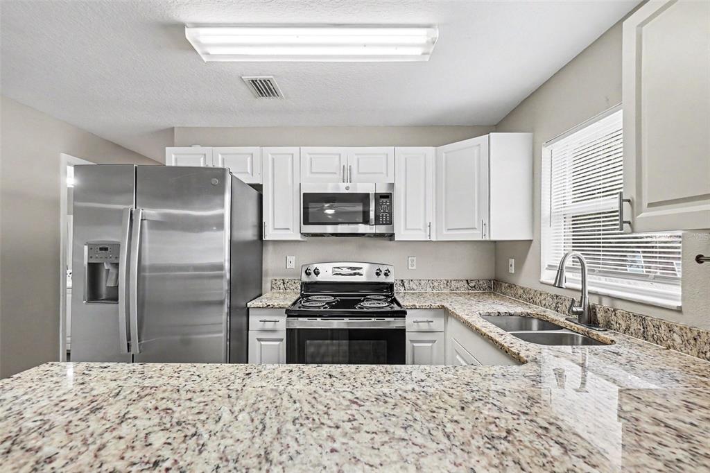 A kitchen features white cabinets, granite countertops, stainless steel appliances, and a double sink — 2608 5TH AVENUE E, PALMETTO, FL