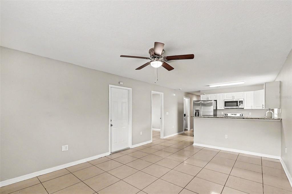 A living room with tile flooring leads to an open kitchen with white cabinets — 2608 5TH AVENUE E, PALMETTO, FL