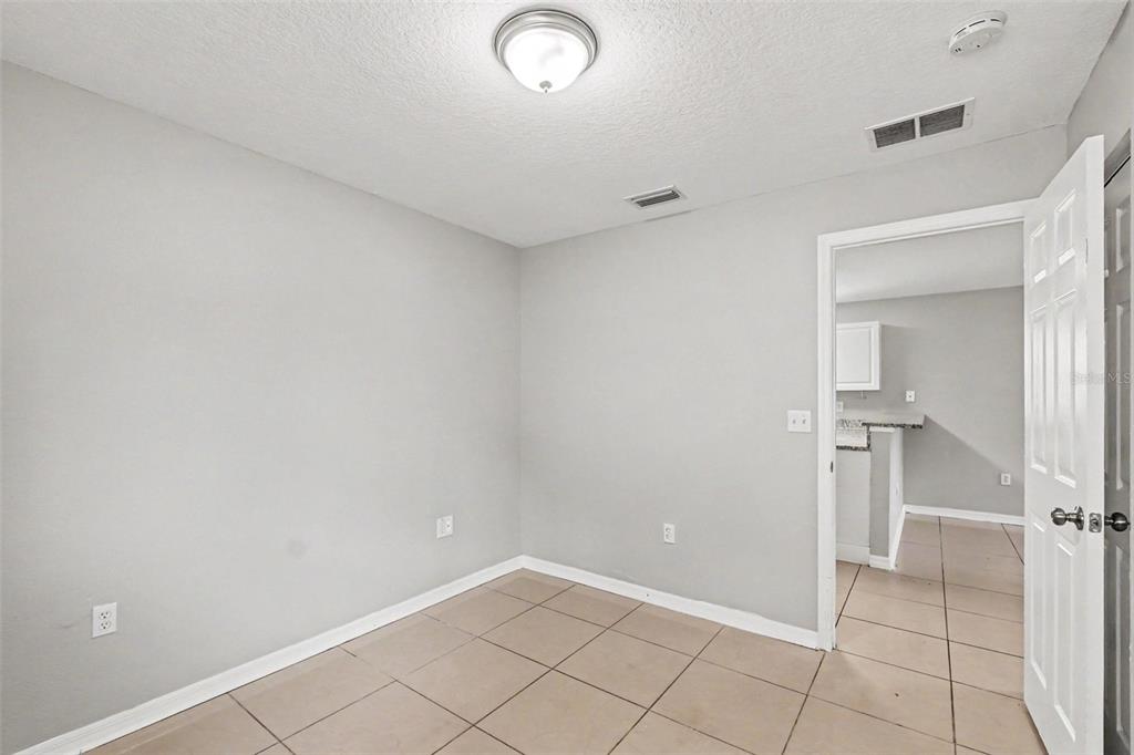 A small, empty room with light gray walls, tile flooring, and a doorway to a kitchen — 2608 5TH AVENUE E, PALMETTO, FL