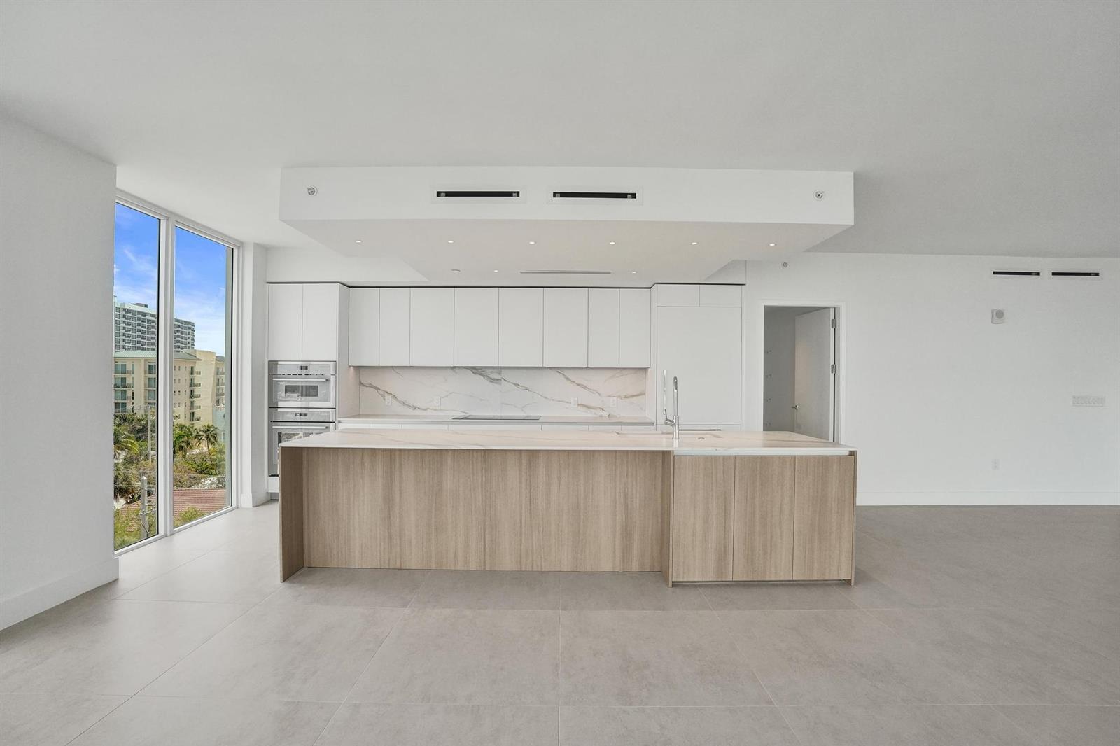 A modern kitchen features white cabinetry, a marble backsplash, and a wood-paneled island — 407 N Riverside Drive # 605, Pompano Beach FL 33062, POMPANO BEACH, FL