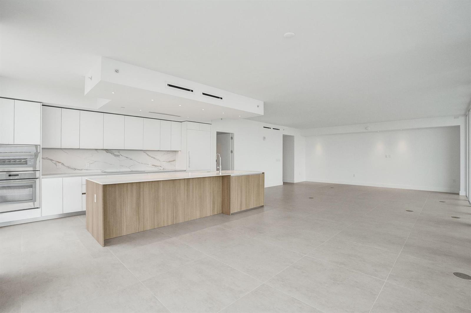A modern kitchen features white cabinetry, a wood-paneled island, and marble backsplash in an open-concept space — 407 N Riverside Drive # 605, Pompano Beach FL 33062, POMPANO BEACH, FL