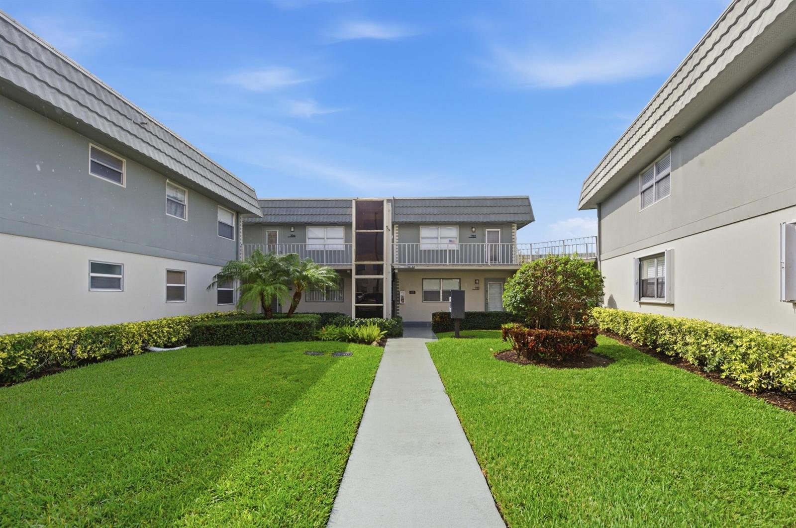 A concrete walkway leads to the entrance of a two-story apartment building with green lawns — 756 Flanders P, Delray Beach FL 33484, DELRAY BEACH, FL