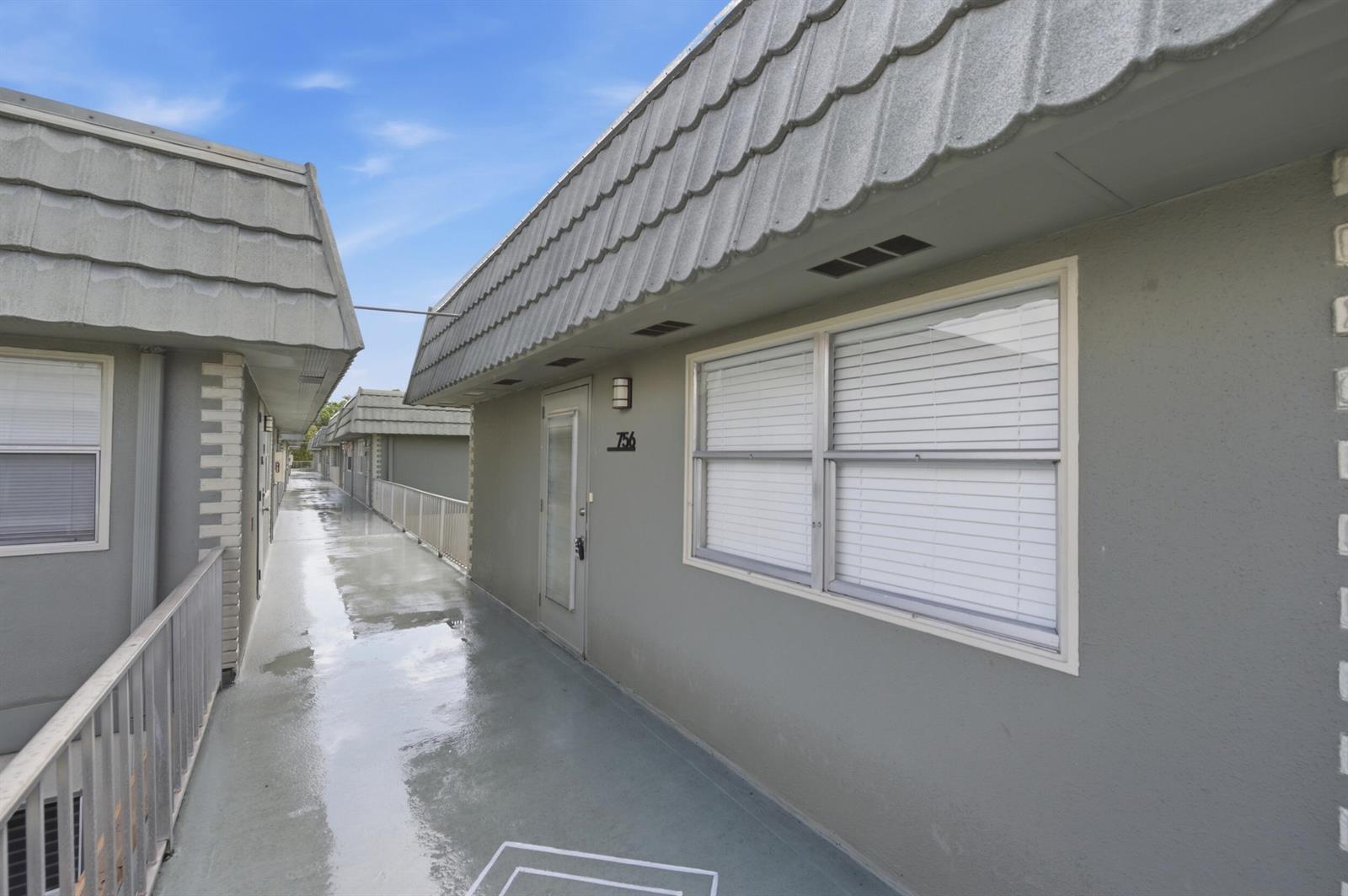 An exterior view of a gray apartment building with a walkway and a numbered door — 756 Flanders P, Delray Beach FL 33484, DELRAY BEACH, FL