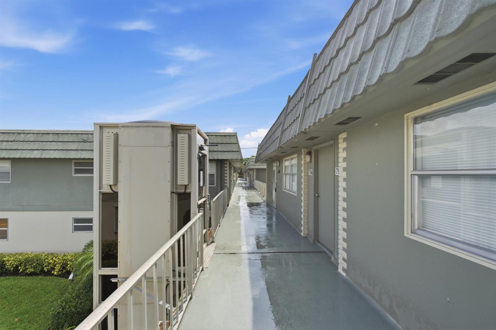 An exterior walkway with a metal railing connects apartment units under a sloped roof — 756 Flanders P, Delray Beach FL 33484, DELRAY BEACH, FL