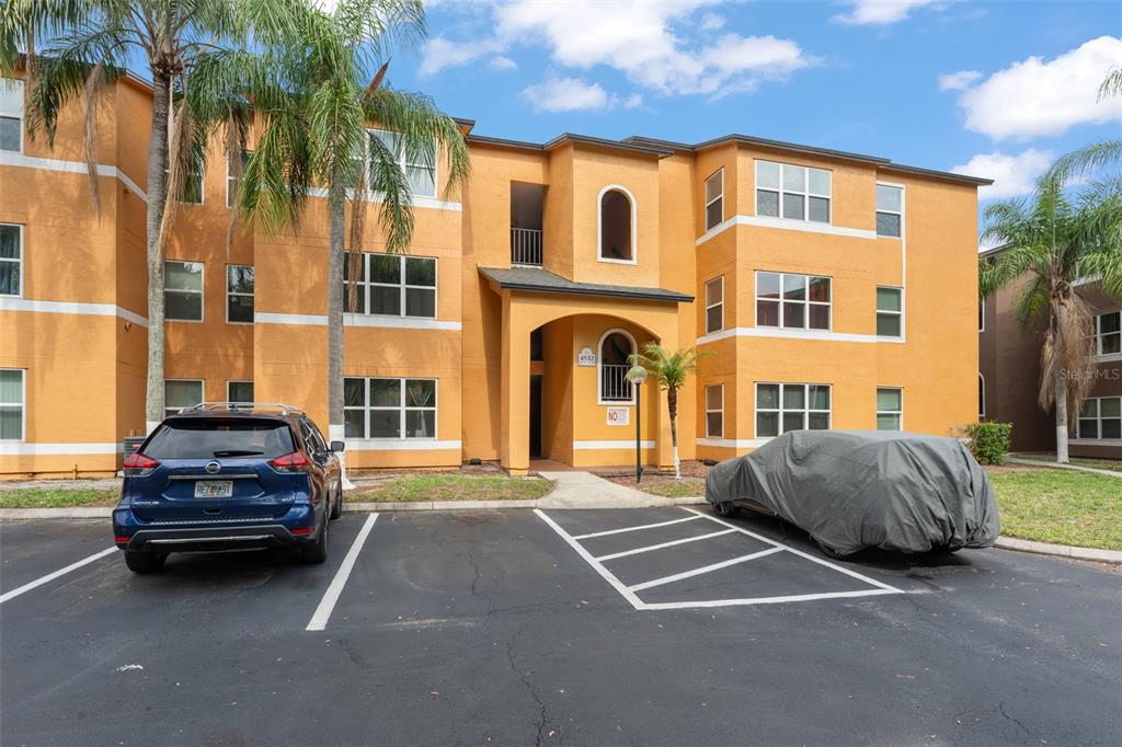 A three-story orange apartment building with a covered entrance and two parked cars — 4532 COMMANDER DRIVE UNIT 2133, ORLANDO, FL