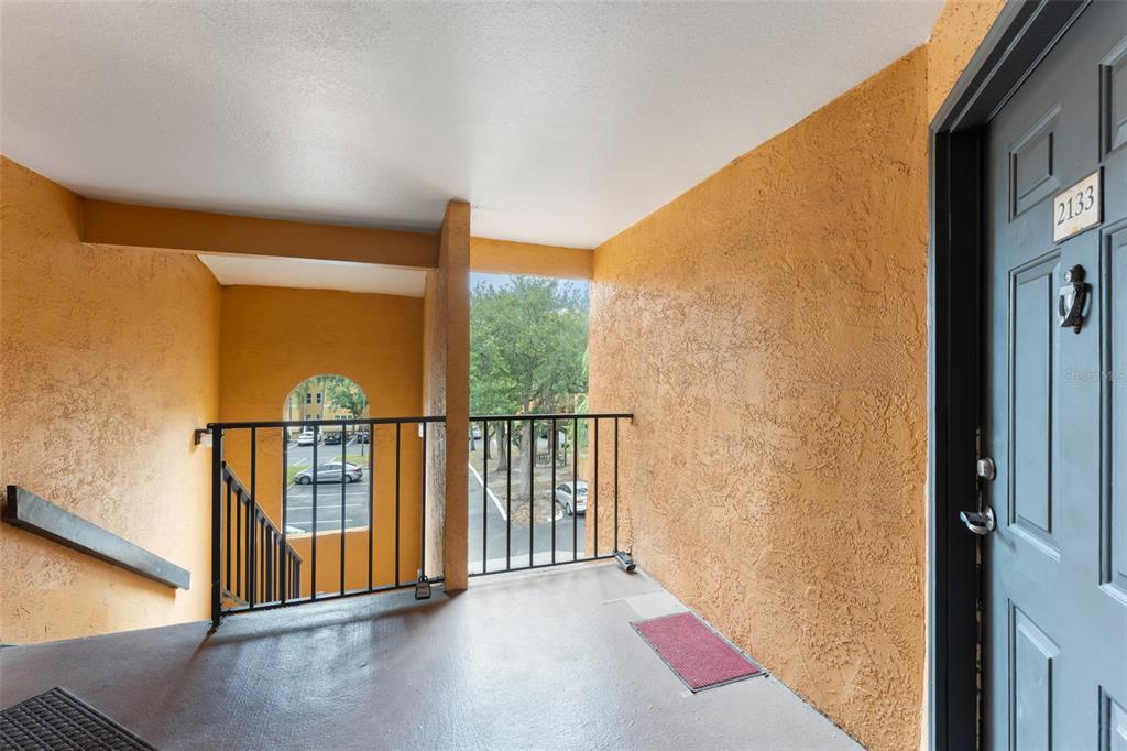 An outdoor apartment entryway features a textured orange wall, a dark door, and metal railings — 4532 COMMANDER DRIVE UNIT 2133, ORLANDO, FL