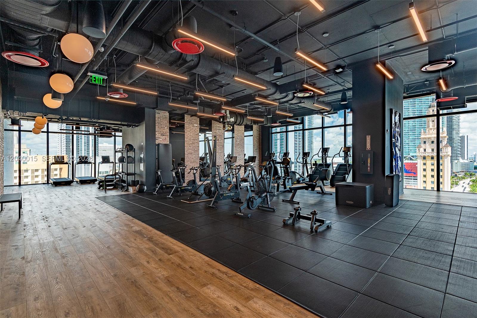 A modern gym features black rubber flooring, wood-look planks, industrial ceilings, and floor-to-ceiling windows — 398 NE 5th St # 2301, Miami FL 33132, MIAMI, FL