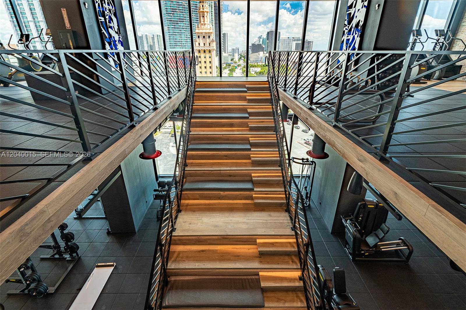 A modern gym features a central wooden staircase with integrated lighting between two elevated platforms — 398 NE 5th St # 2301, Miami FL 33132, MIAMI, FL