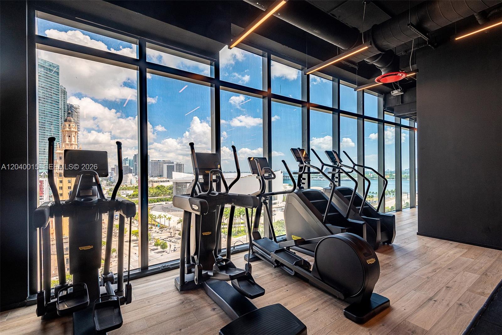 A gym features several elliptical machines and stair climbers facing floor-to-ceiling windows overlooking a city — 398 NE 5th St # 2301, Miami FL 33132, MIAMI, FL