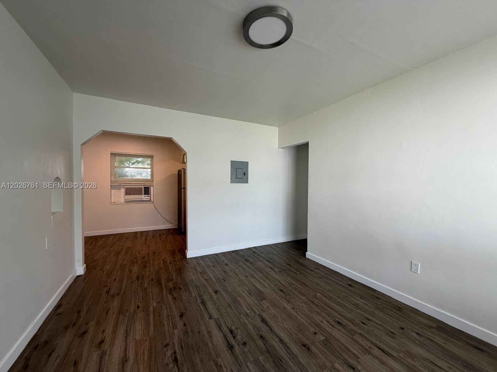 A living room with wood-look flooring leads through an arched doorway to a kitchen area — 541 SW 7th St # 3, Miami FL 33130, MIAMI, FL