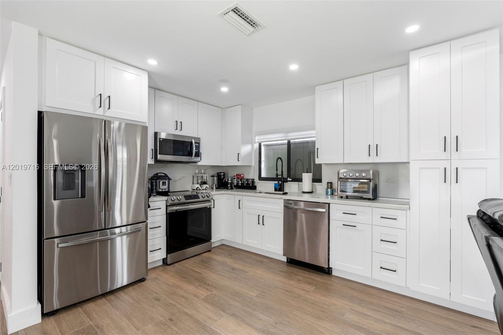 A modern kitchen features white shaker cabinets, stainless steel appliances, and light wood-look flooring — 9460 Haitian Dr, Cutler Bay FL 33189, CUTLER BAY, FL