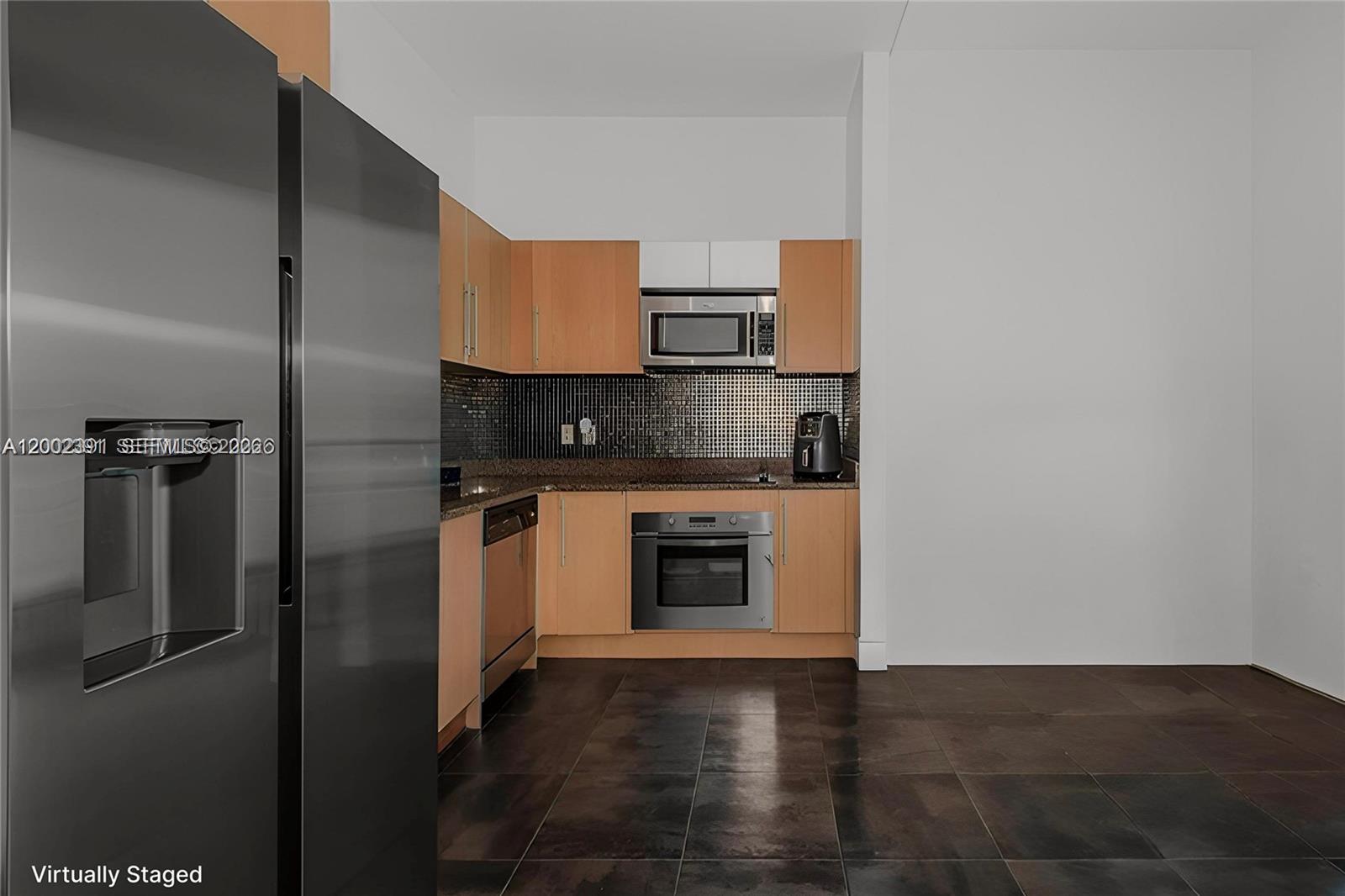 A kitchen features light wood cabinets, stainless steel appliances, dark tile flooring, and a backsplash — 300 S Biscayne Blvd # 3903, Miami FL 33131, MIAMI, FL