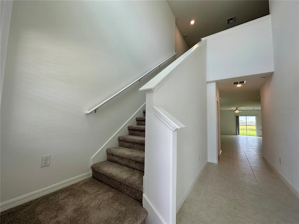 A carpeted staircase with a white railing sits beside a tiled hallway leading to a room — 11131 RADIANT SHORE LOOP, SAN ANTONIO, FL