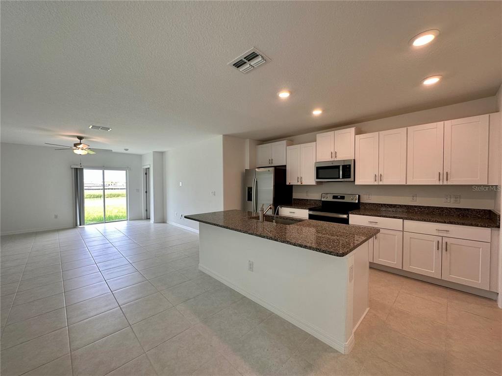 A kitchen with white cabinets and granite countertops opens into a tiled living area — 11131 RADIANT SHORE LOOP, SAN ANTONIO, FL