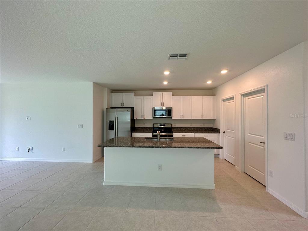 A kitchen features white cabinets, granite countertops, a center island, and stainless steel appliances — 11131 RADIANT SHORE LOOP, SAN ANTONIO, FL