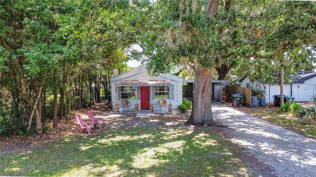 A single-story house with a red front door sits under large trees with a gravel driveway — 1014 MEADOWS AVENUE, ORLANDO, FL