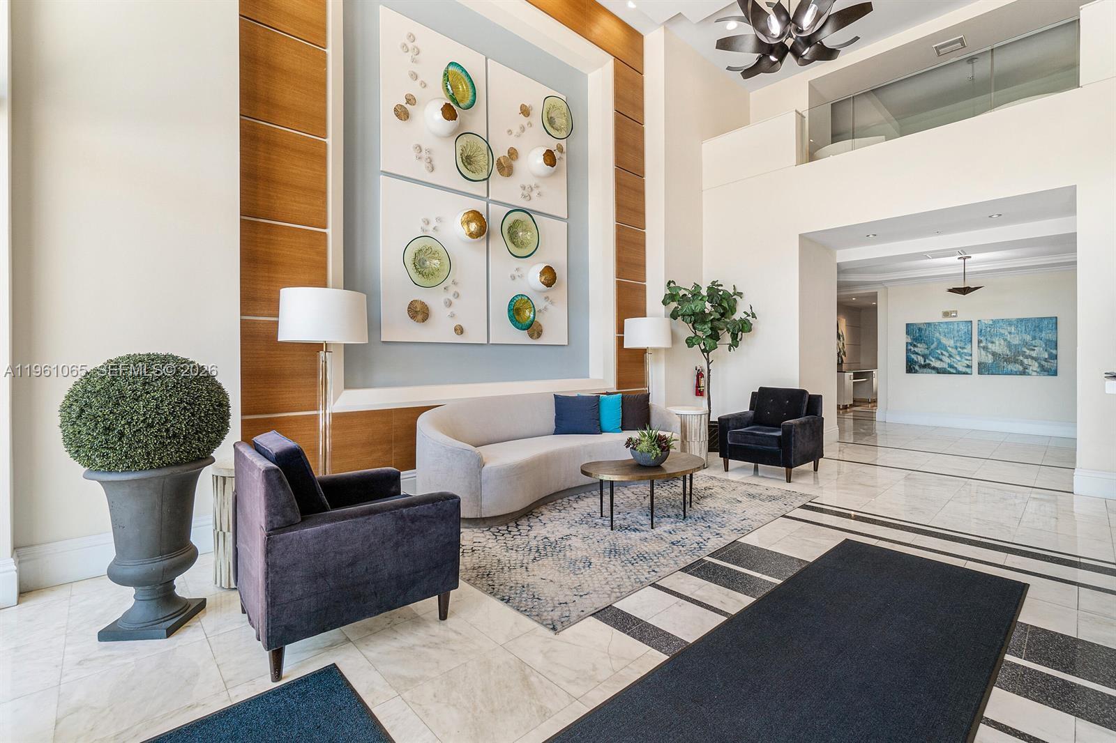 A modern lobby features a curved sofa, armchairs, and decorative wall art under high ceilings — 700 E Boynton Beach Blvd # 1007, Boynton Beach FL 33435, BOYNTON BEACH, FL