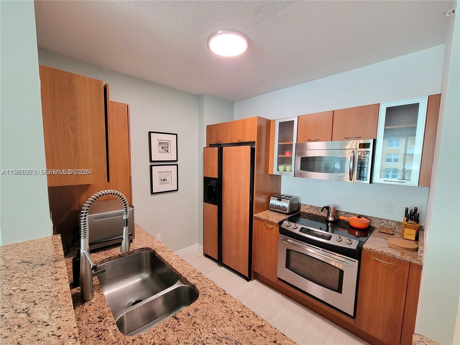 A kitchen features wood cabinets, granite countertops, stainless steel appliances, and a double-basin sink — 700 E Boynton Beach Blvd # 1007, Boynton Beach FL 33435, BOYNTON BEACH, FL