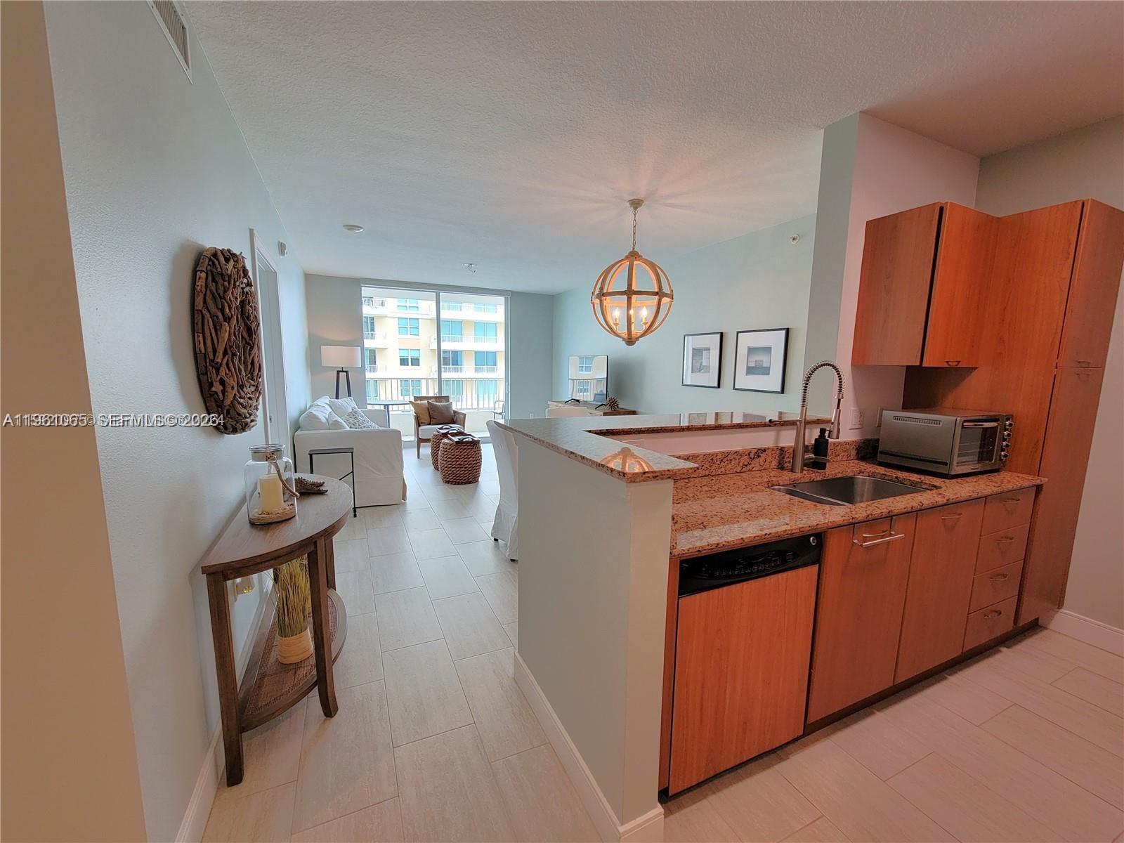 A kitchen with wood cabinets and granite countertops overlooks an open-concept living and dining area — 700 E Boynton Beach Blvd # 1007, Boynton Beach FL 33435, BOYNTON BEACH, FL
