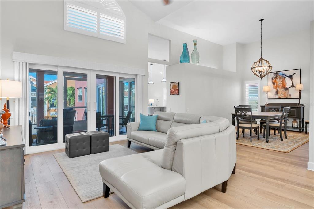 A bright living and dining area features light wood floors, vaulted ceilings, and sliding doors — 18 JEFFERSON COURT S, ST PETERSBURG, FL