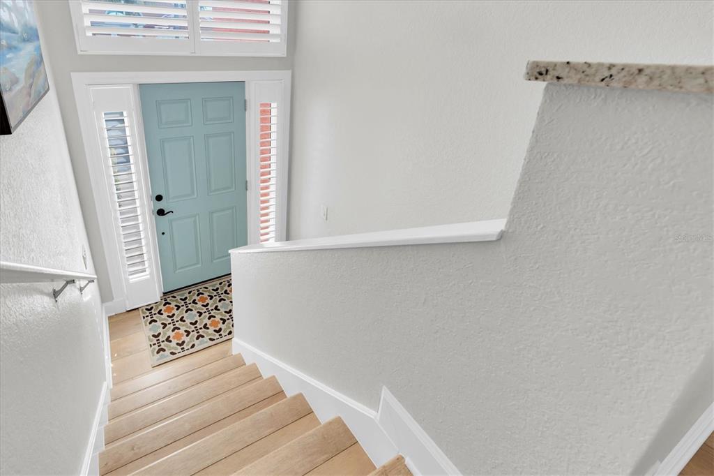A view looking down a wooden staircase toward a light blue front door and entryway — 18 JEFFERSON COURT S, ST PETERSBURG, FL