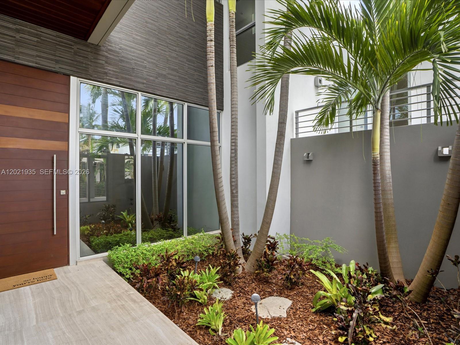 A modern home entrance features a wooden door, large glass windows, and a landscaped courtyard — 125 Hampton Ln, Key Biscayne FL 33149, KEY BISCAYNE, FL