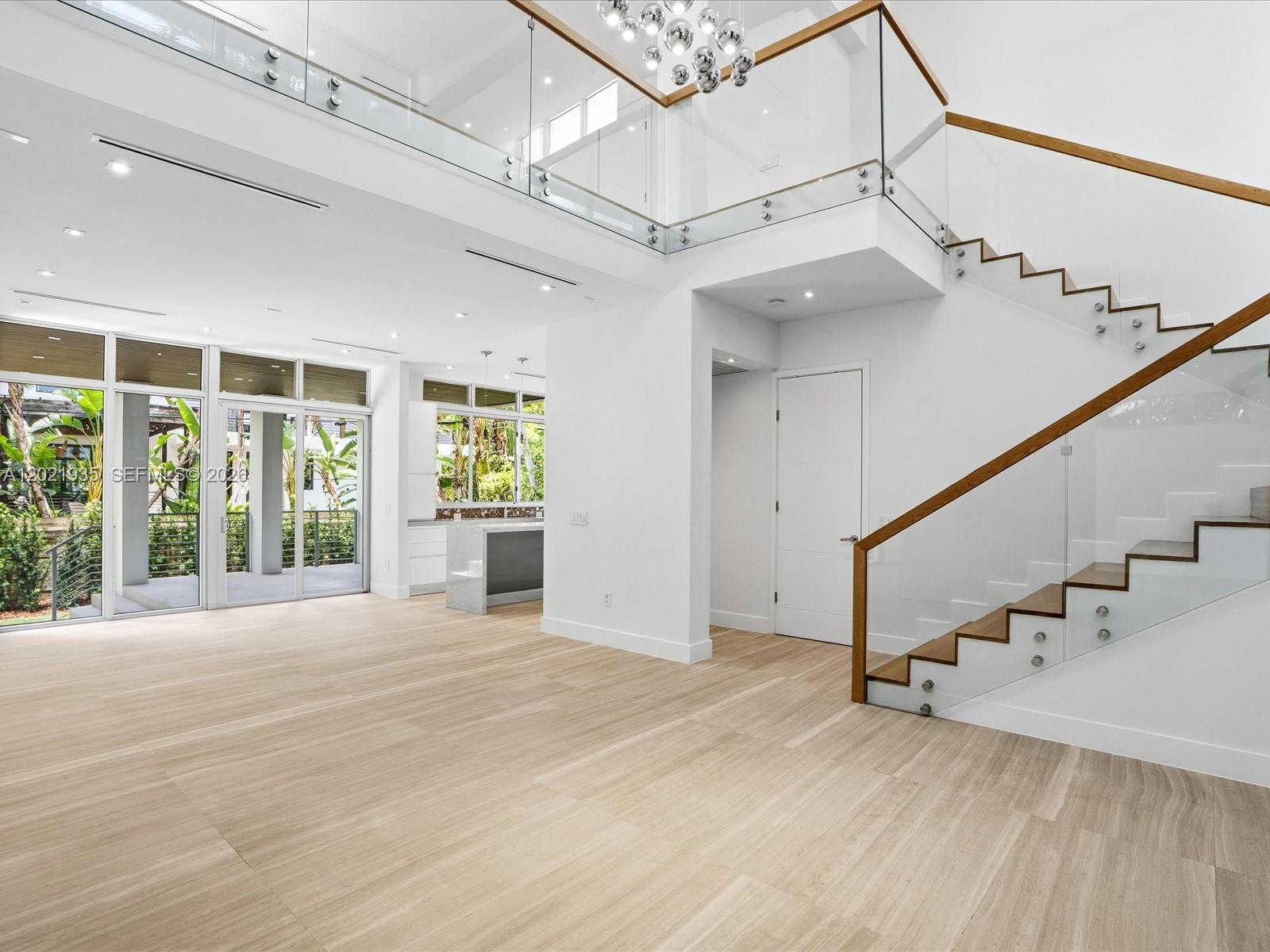 A modern, open-concept living area features light wood flooring, a glass-railed staircase, and high ceilings — 125 Hampton Ln, Key Biscayne FL 33149, KEY BISCAYNE, FL