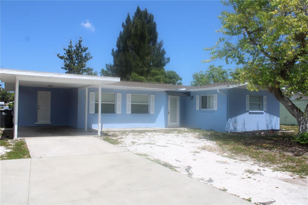 A light blue single-story house features a concrete driveway, a carport, and white shutters — 3316 W 26TH STREET, BRADENTON, FL