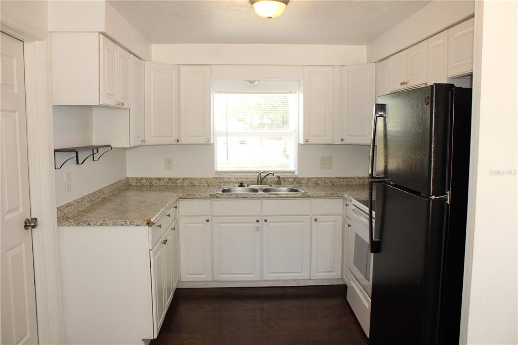 A kitchen with white cabinets, granite-look countertops, a black refrigerator, and dark wood flooring — 3316 W 26TH STREET, BRADENTON, FL