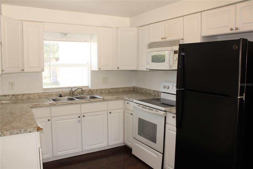 A kitchen with white cabinets, granite countertops, a white stove, and a black refrigerator — 3316 W 26TH STREET, BRADENTON, FL