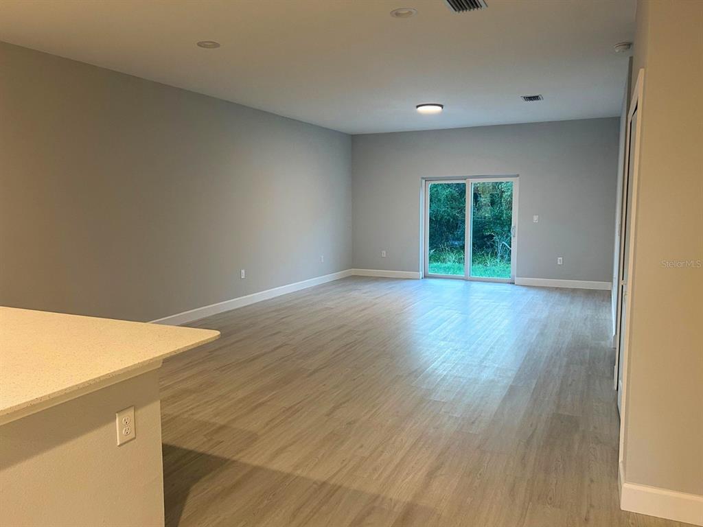 An empty living room features light wood-look flooring, gray walls, and a sliding glass door — 10385 PORT EVERGLADES STREET, PORT CHARLOTTE, FL