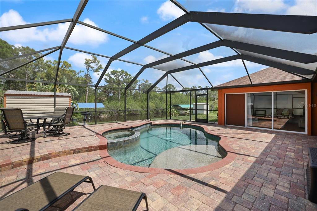 A screened-in patio features a paver deck, a swimming pool with a spa, and furniture — 20 CORY STREET, PORT CHARLOTTE, FL