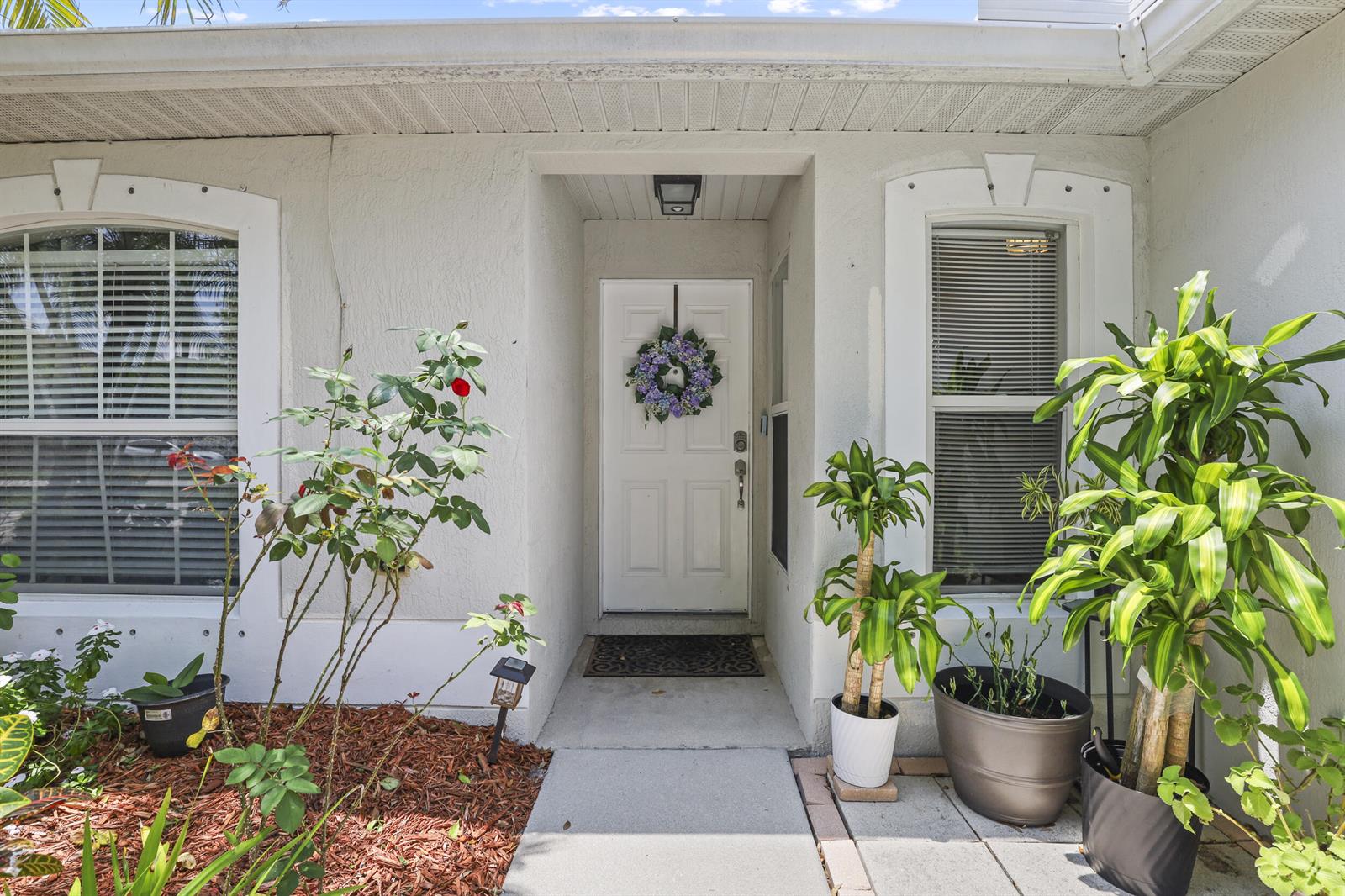 The exterior of a house features a white front door, two windows, and potted plants — 2631 12th Square SW, Vero Beach FL 32968, VERO BEACH, FL