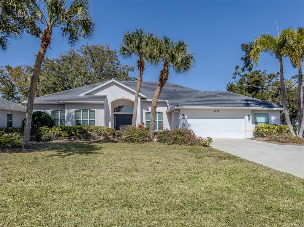 A single-story house with a tiled roof, white garage, and palm trees in the front yard — 2139 CALUSA LAKES BOULEVARD, NOKOMIS, FL