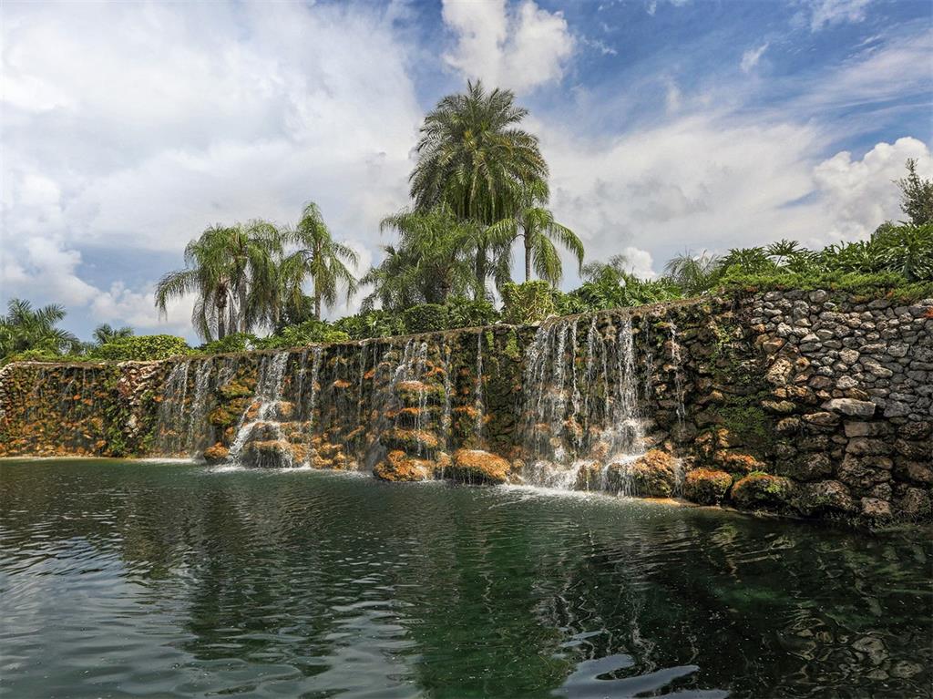 A stone waterfall flows into a pond surrounded by lush greenery and palm trees — 2139 CALUSA LAKES BOULEVARD, NOKOMIS, FL