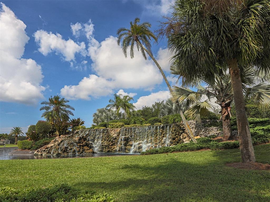 A stone waterfall feature sits in a landscaped garden with palm trees and a pond — 2139 CALUSA LAKES BOULEVARD, NOKOMIS, FL