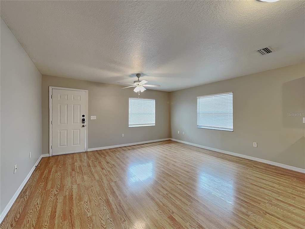 An empty living room features light wood flooring, beige walls, a ceiling fan, and two windows — 2835 31ST AVENUE E, BRADENTON, FL