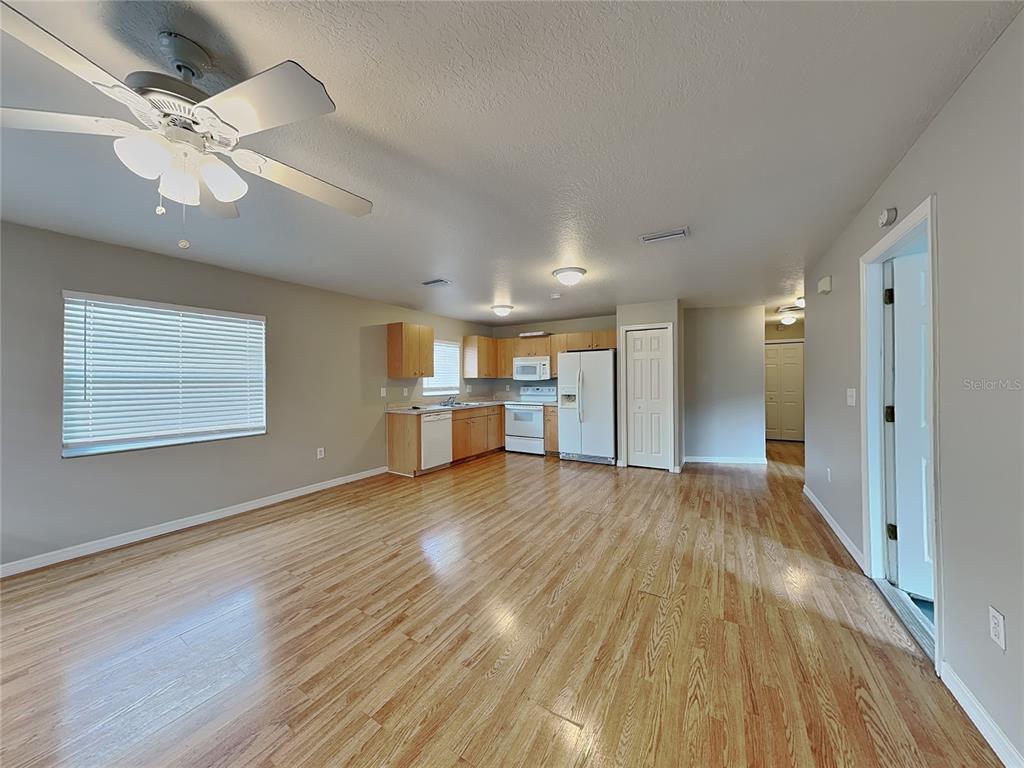 An open-concept kitchen and living area features light wood flooring and white appliances — 2835 31ST AVENUE E, BRADENTON, FL