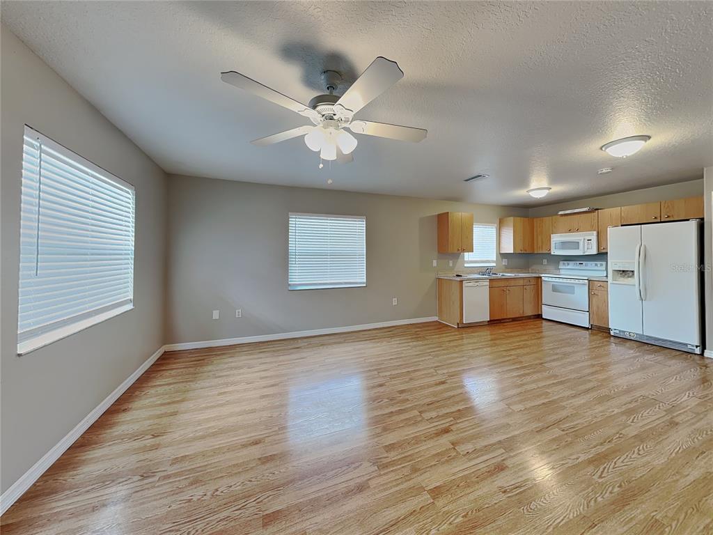 An open-concept kitchen and living area features light wood flooring, beige walls, and white appliances — 2835 31ST AVENUE E, BRADENTON, FL