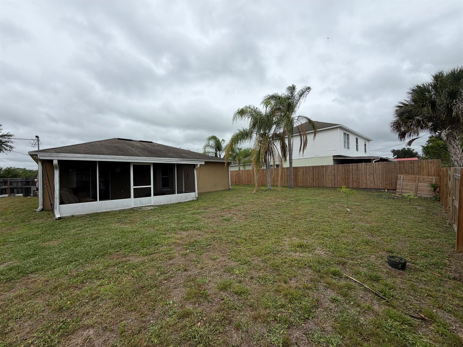 A backyard features a screened-in patio, a wooden fence, and palm trees under a cloudy sky — 3426 NW 38th Avenue # 3426, Okeechobee FL 34972, OKEECHOBEE, FL