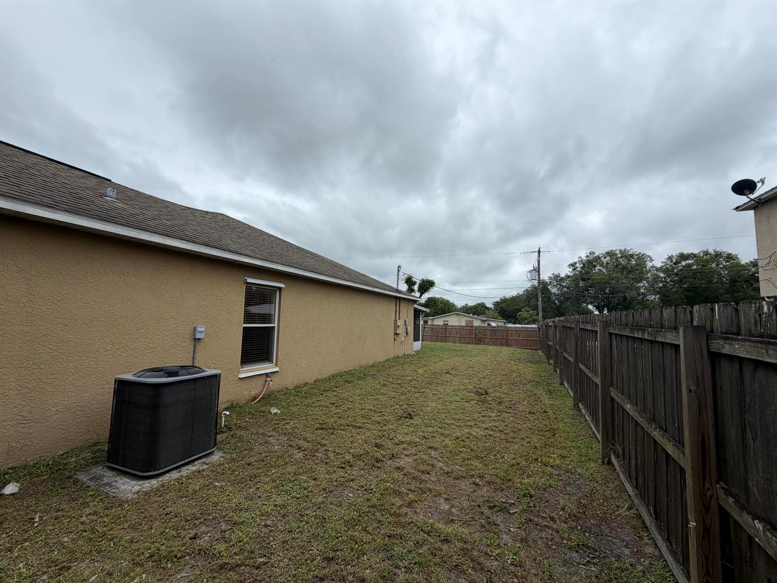 A side yard features a tan stucco house wall, an HVAC unit, and a wooden fence — 3426 NW 38th Avenue # 3426, Okeechobee FL 34972, OKEECHOBEE, FL