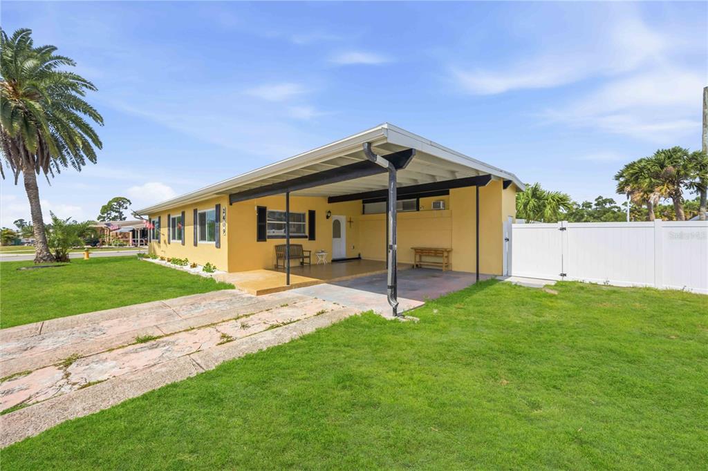 A yellow single-story house features a covered carport, a concrete driveway, and a white fence — 2409 EDNOR STREET, PORT CHARLOTTE, FL