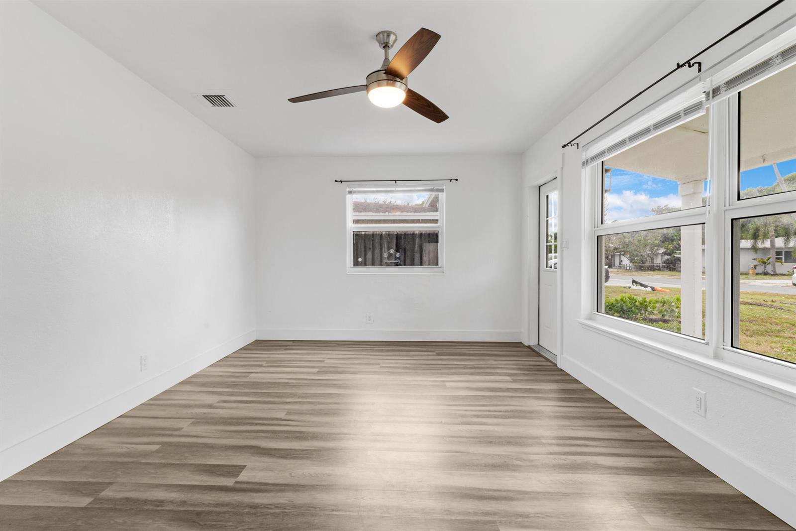 An empty room features white walls, wood-look flooring, a ceiling fan, and large windows — 508 NE 12th Avenue, Pompano Beach FL 33060, POMPANO BEACH, FL